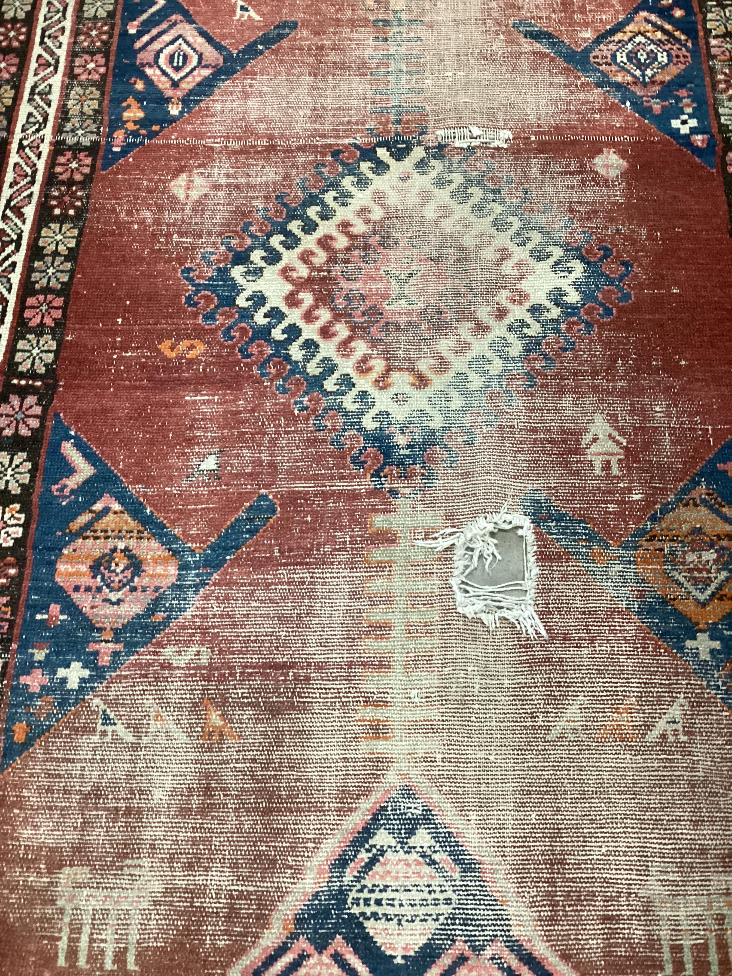 An Antique Caucasian brick red ground runner 336cm x 110cm, severely worn and holed